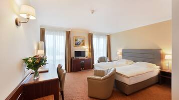 A hotel room with two beds, a desk with a computer, a chair, a TV, and a painting on the wall.