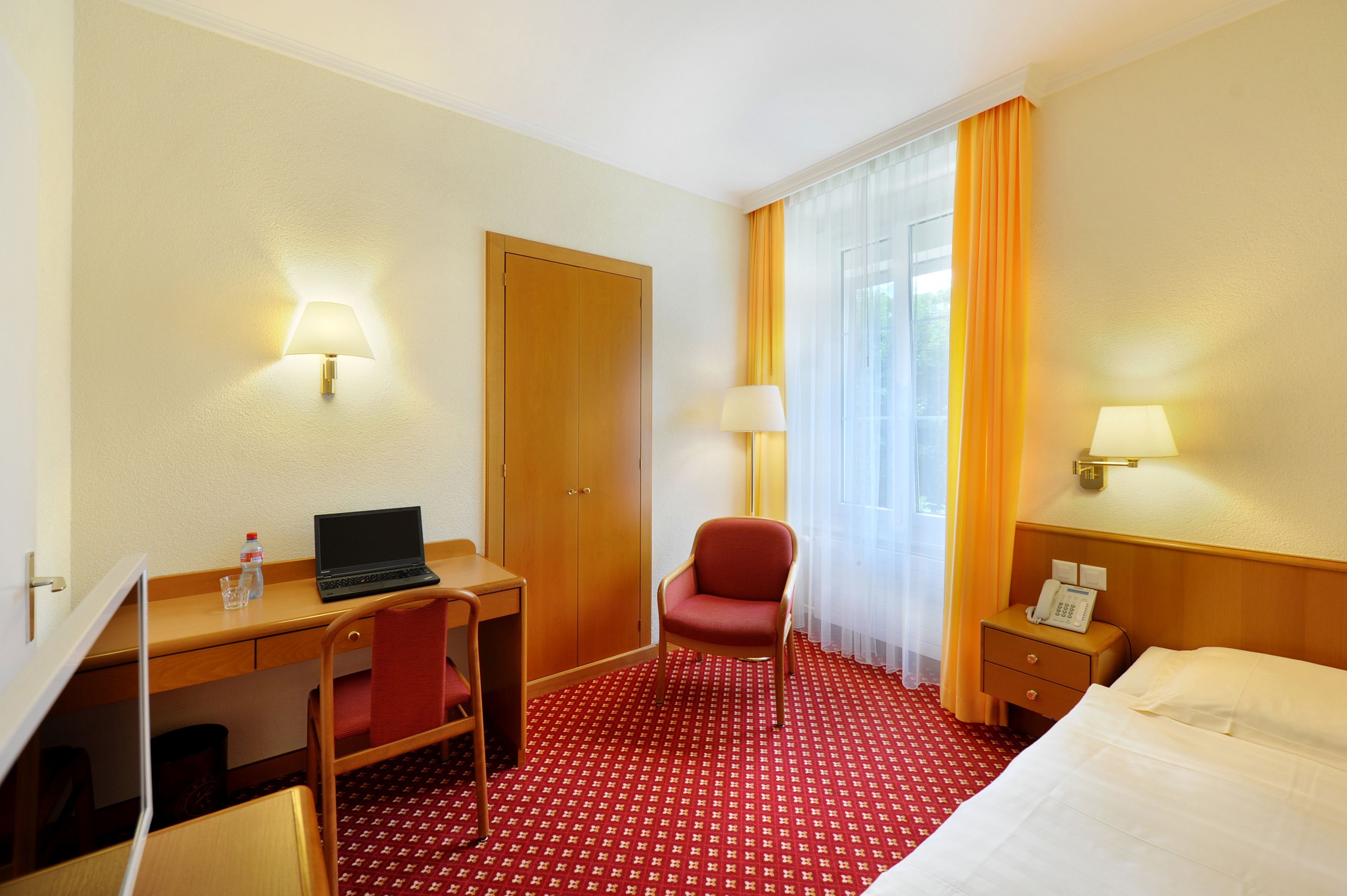 A hotel room with a desk, chair, bed, and a small table with a phone.