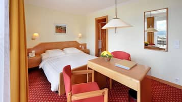 A hotel room with a bed, desk, chairs, and a mirror.