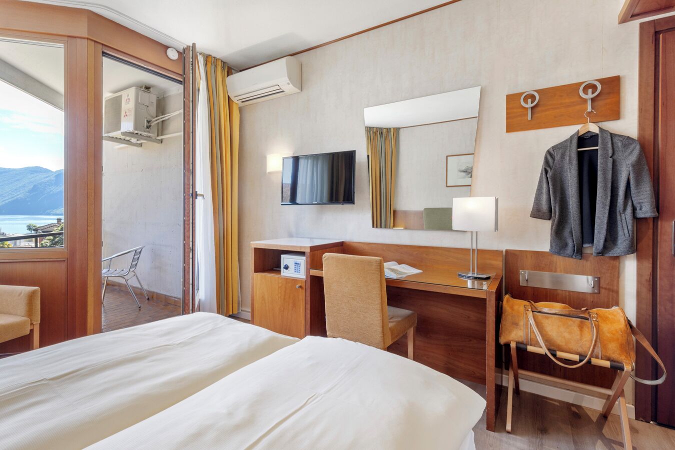Una habitación de hotel con cama, escritorio, silla, televisor y vistas al exterior.