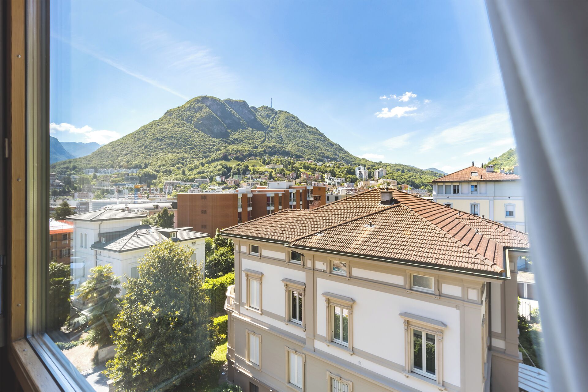 Une vue depuis une fenêtre donnant sur un paysage urbain, avec une montagne en arrière-plan.