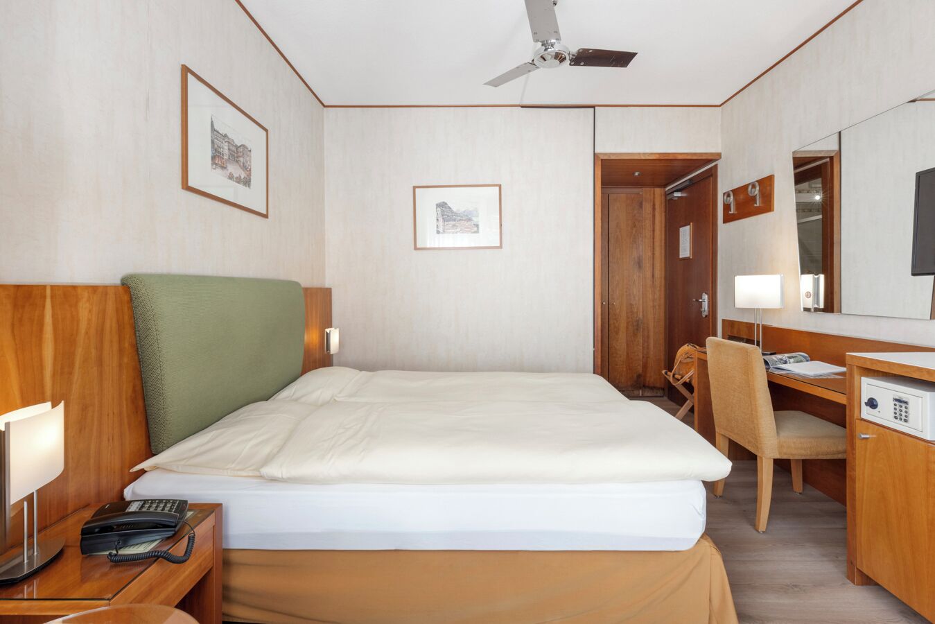 Ett hotellrum med en säng, ett skrivbord, en stol, en telefon och en takfläkt.