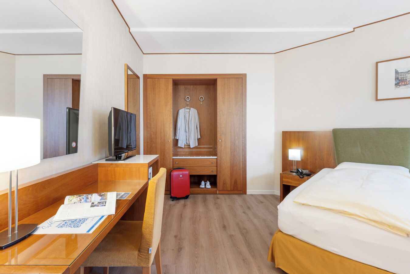 Una habitación de hotel con cama, escritorio con computadora, televisión, armario y maleta.