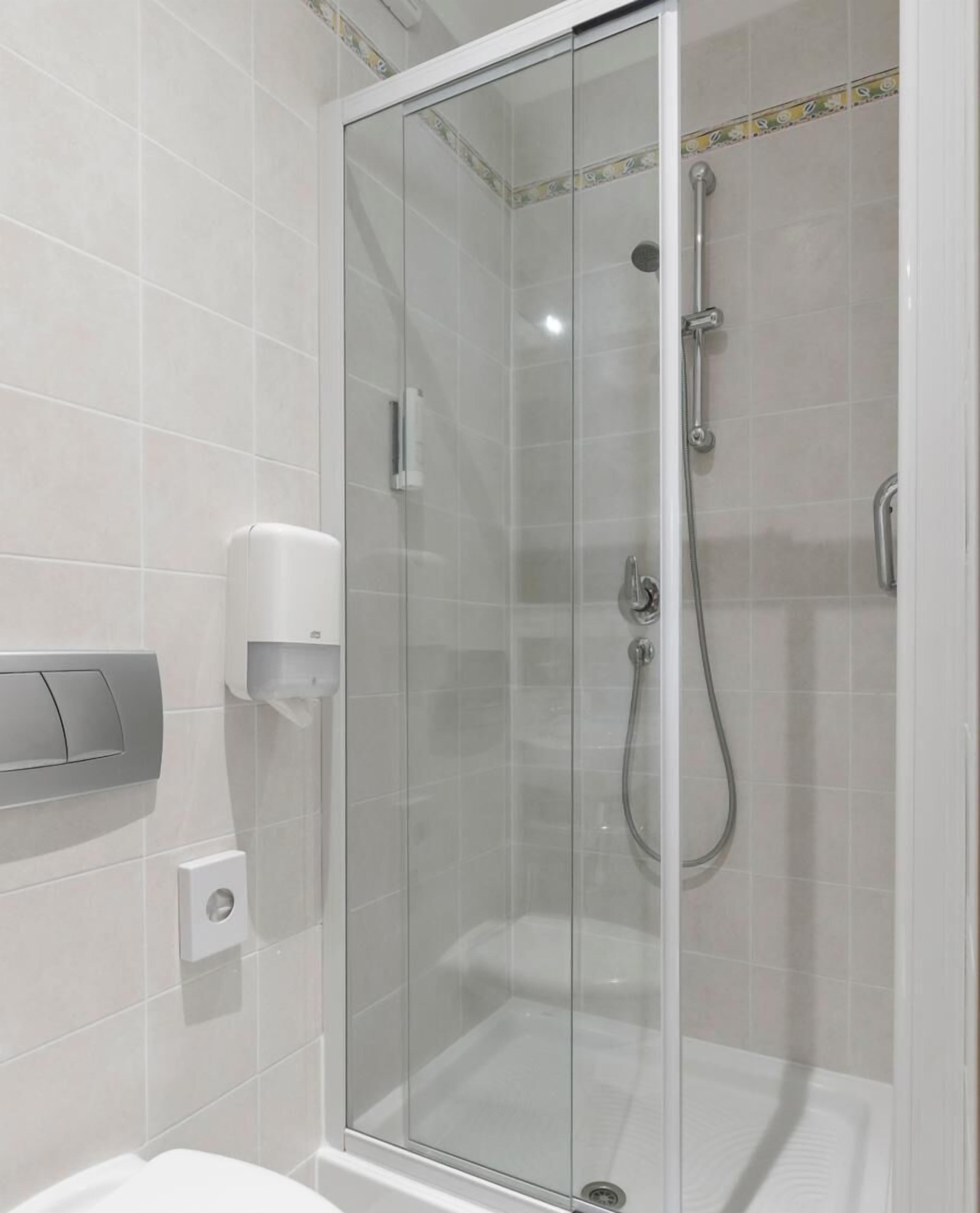 A glass-enclosed shower stall with a handheld showerhead and a wall-mounted hand dryer.