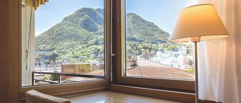 Habitación de hotel con un amplio ventanal que ofrece vistas a una montaña y al paisaje urbano.