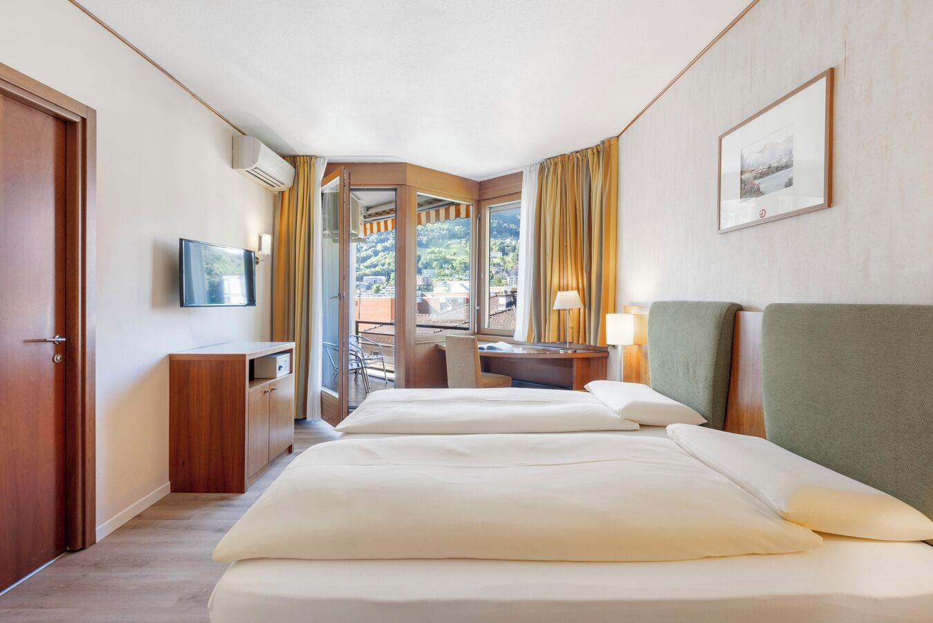 Ein Hotelzimmer mit zwei Betten, einem Schreibtisch, einem Stuhl, einem Fernseher und einem Fenster mit Vorhängen.