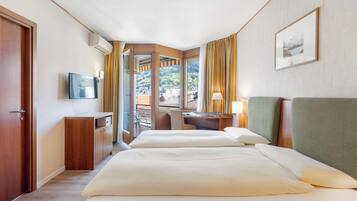 Habitación de hotel con dos camas, un escritorio, una silla, un televisor y una ventana con cortinas.
