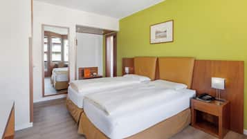 A hotel room with two beds, a wooden headboard, a bedside table with a lamp, and a framed picture on the wall.