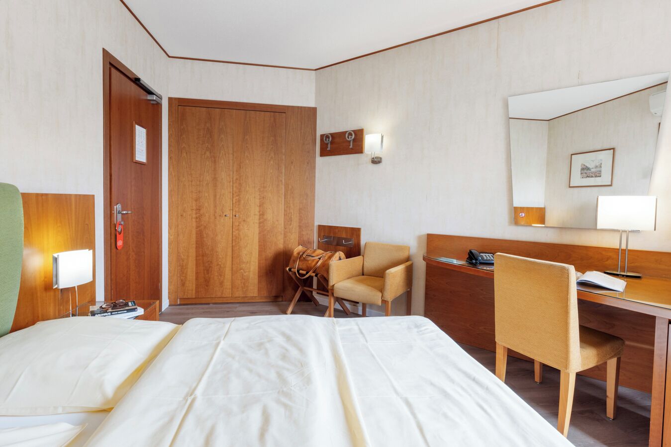 A hotel room with a bed, a desk, a chair, a wardrobe, and a mirror.