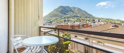 A balcony with a table and chairs, overlooking a cityscape and a mountain.