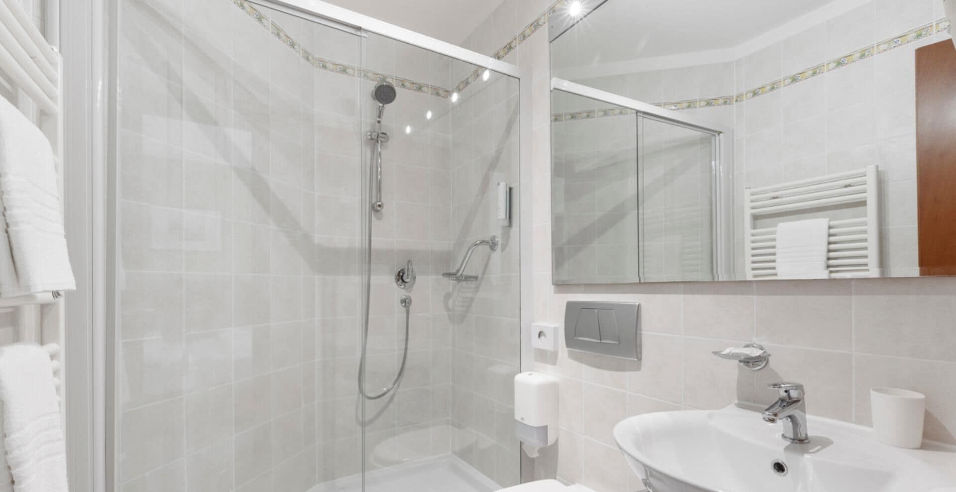 Un baño moderno con ducha envuelta en vidrio, un lavamanos blanco y un espejo sobre él.
