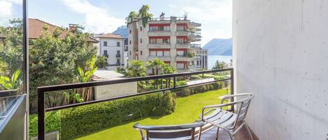 Un balcón con dos sillas y vista a un jardín verde, con un edificio que tiene balcones al fondo.