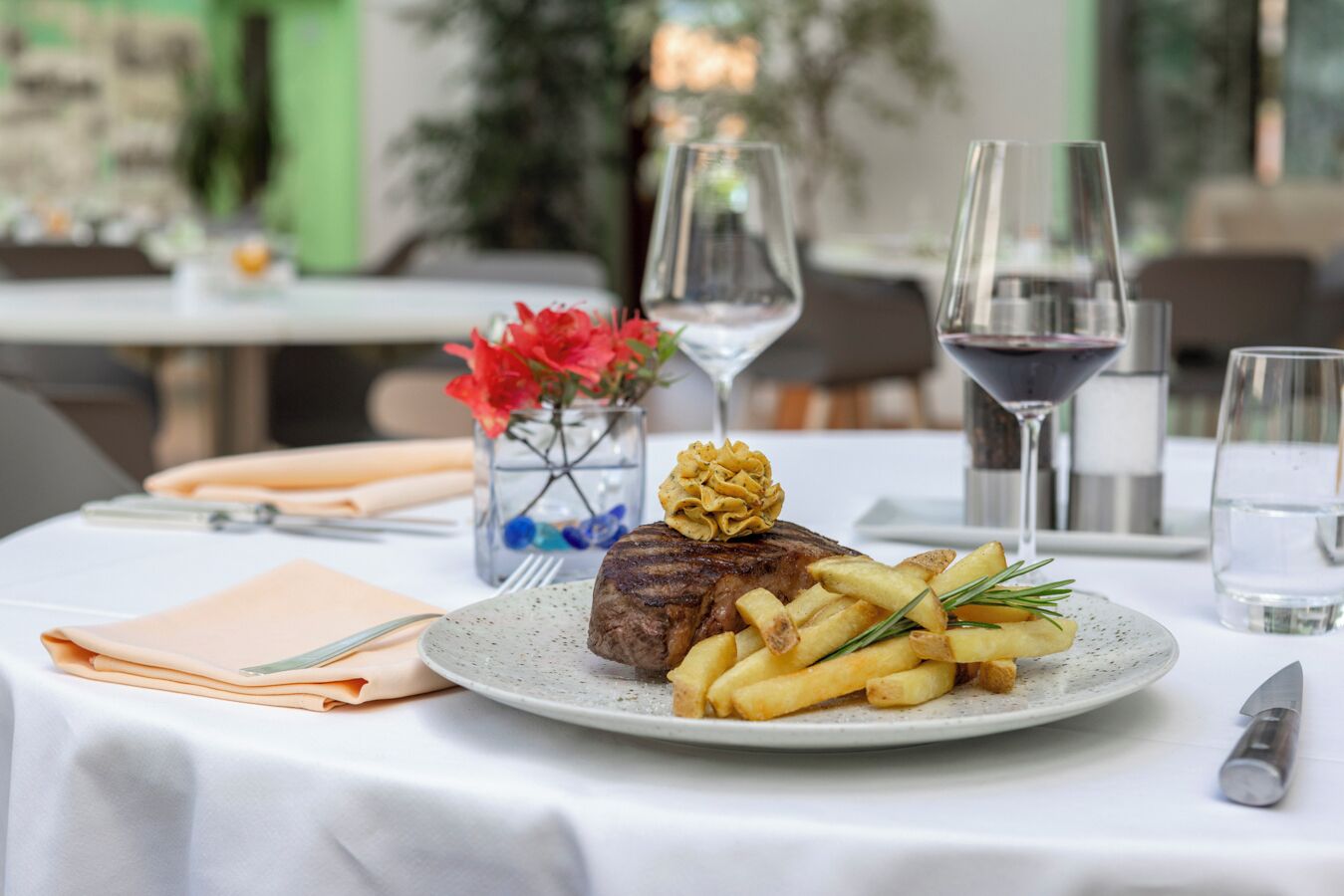 Une table à manger avec un steak, des frites et un arrangement floral décoratif.