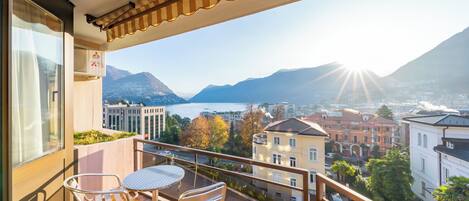 Een balkon met een tafel en stoelen, met uitzicht op een prachtig meer en bergen.