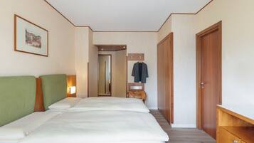 A hotel room with two beds, a wooden wardrobe, a coat rack, and a framed picture on the wall.