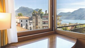 Habitación de esquina con un ventanal grande que ofrece vistas a edificios, montañas y un lago.