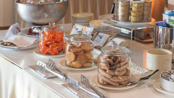 Une table de buffet garnie de divers aliments, notamment des bocaux de biscuits et de pâtisseries, et un grand saladier en arrière-plan.