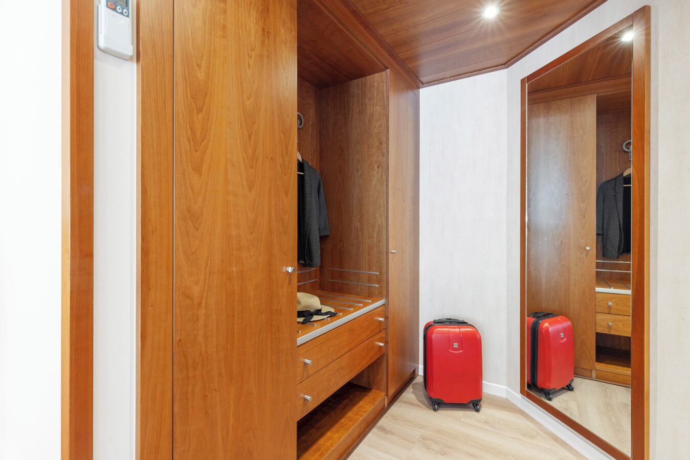 Ein begehbarer Kleiderschrank mit Holztüren, einem Spiegel und einem roten Koffer.