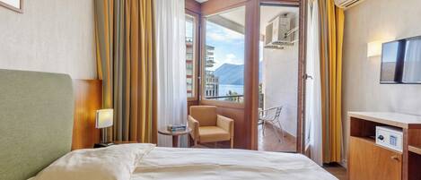 Habitación de hotel con cama, escritorio, silla, una mesita y balcón con vistas a montañas.