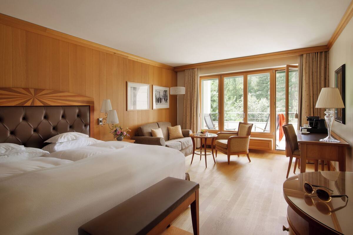 A hotel room with a large bed, a sofa, a desk, and a dining area.
