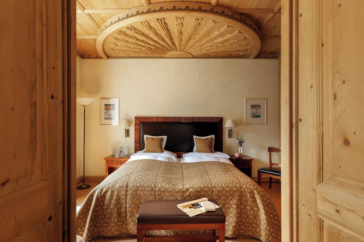 A wooden-paneled room with a large bed, a wooden bench, and a ceiling fan.