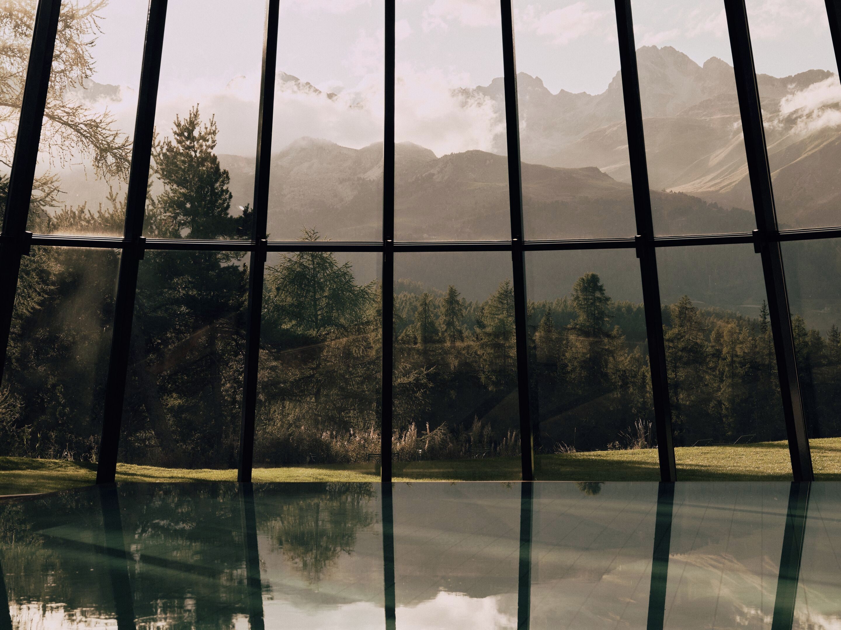 Une vue à travers une fenêtre, avec le reflet d’arbres et de montagnes.