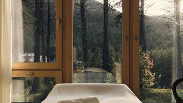 Ein Schlafzimmer mit einem Bett, einem Fenster und Blick auf einen Wald.