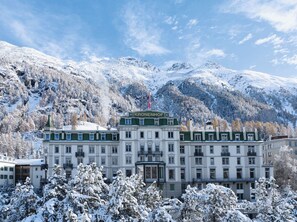 Ein großes, mehrgeschossiges Gebäude mit einer grün-weißen Fassade, mit der Aufschrift "KRONENHOF", umgeben von schneebedeckten Bäumen und Bergen im Hintergrund.