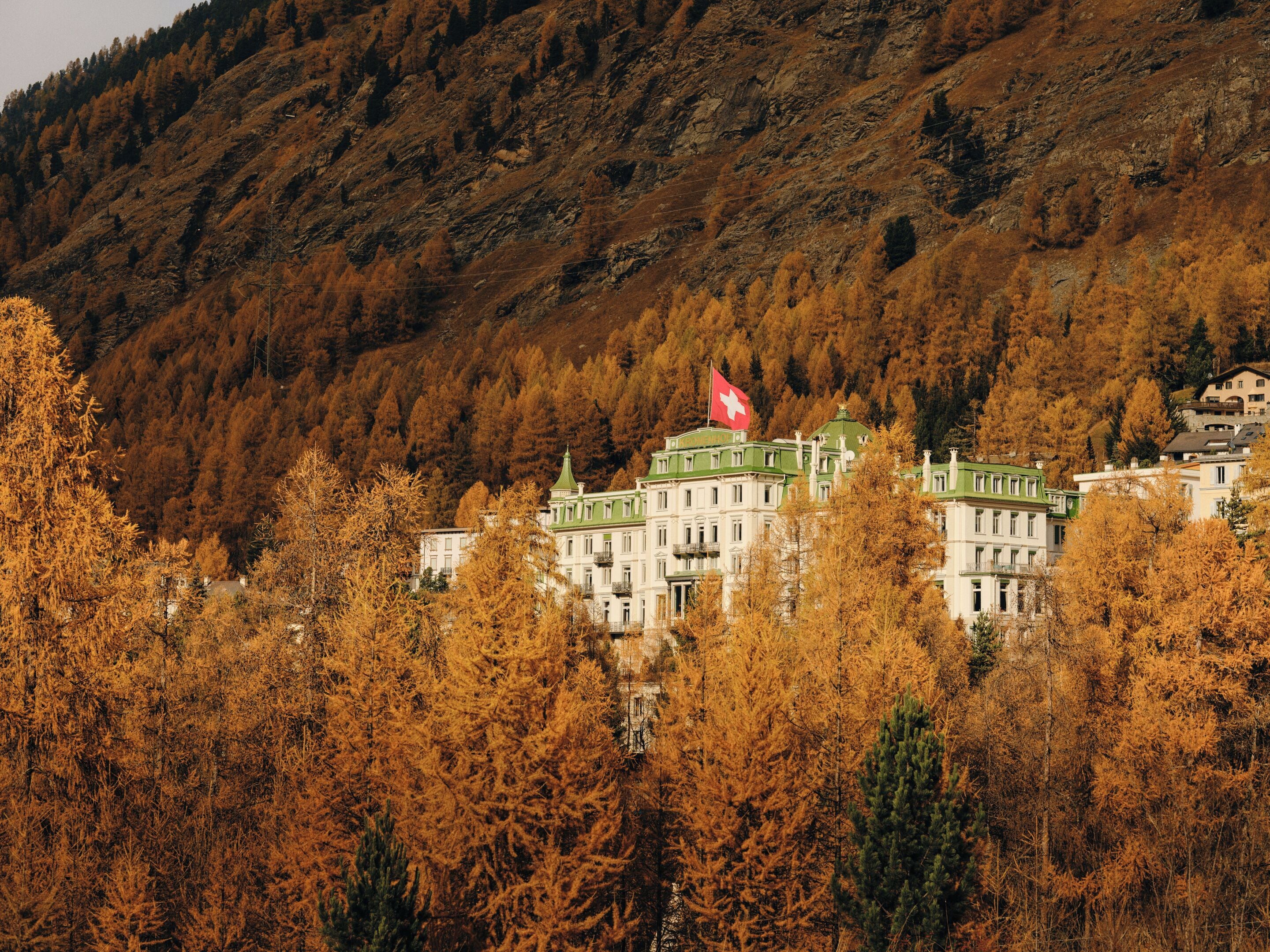 A building with a green roof and a red flag, surrounded by autumn trees.