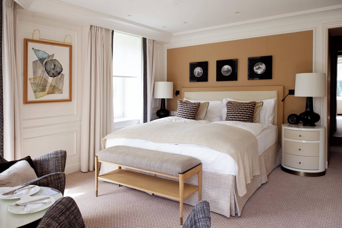 A neatly arranged hotel room with a large bed, bedside tables, a bench, and a dining area.