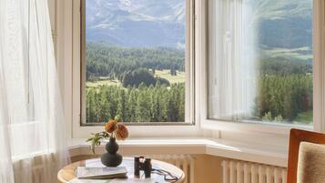 Una habitación con vistas a montañas, una mesa con un jarrón de flores, una silla con un sombrero y un radiador.