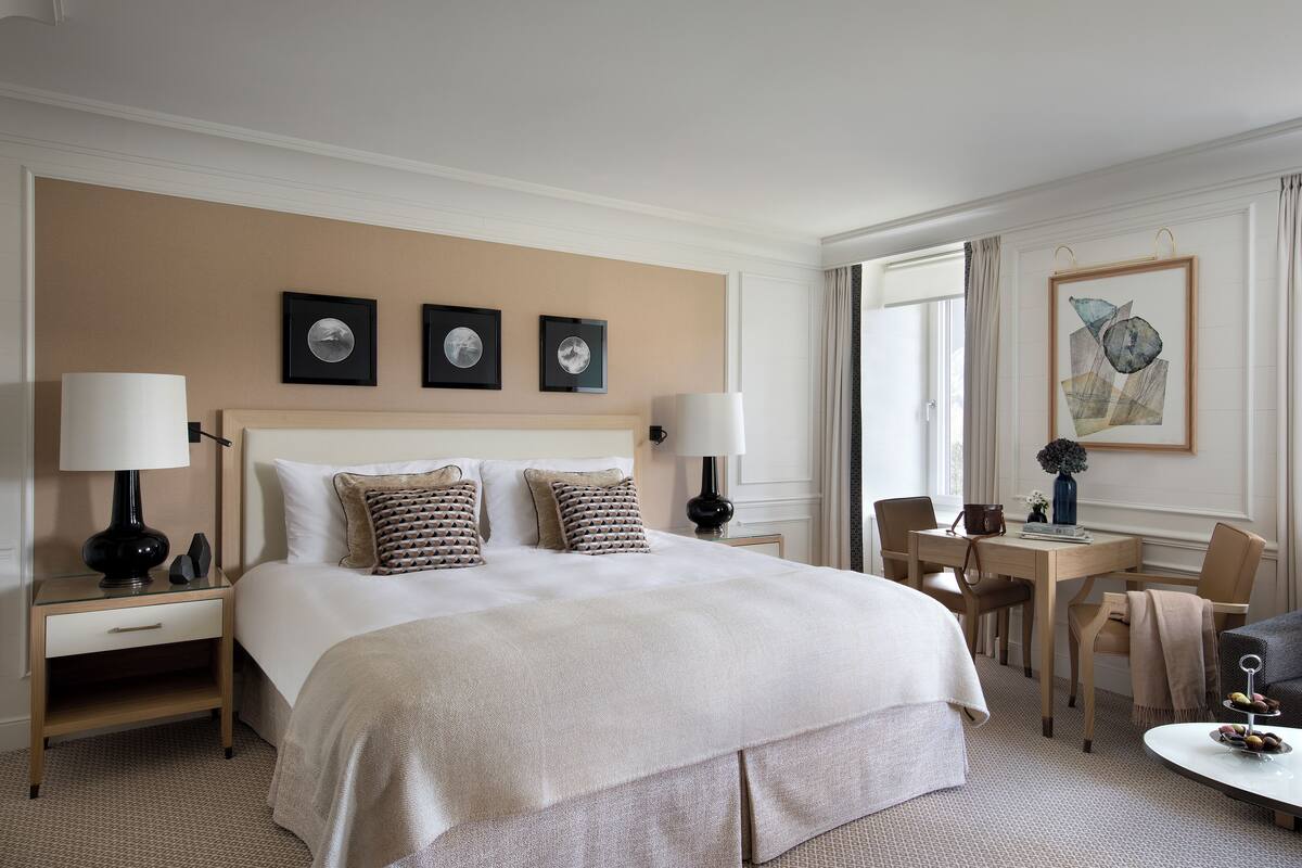 A hotel room with a large bed, two bedside tables with lamps, a small desk, a chair, and a round coffee table.