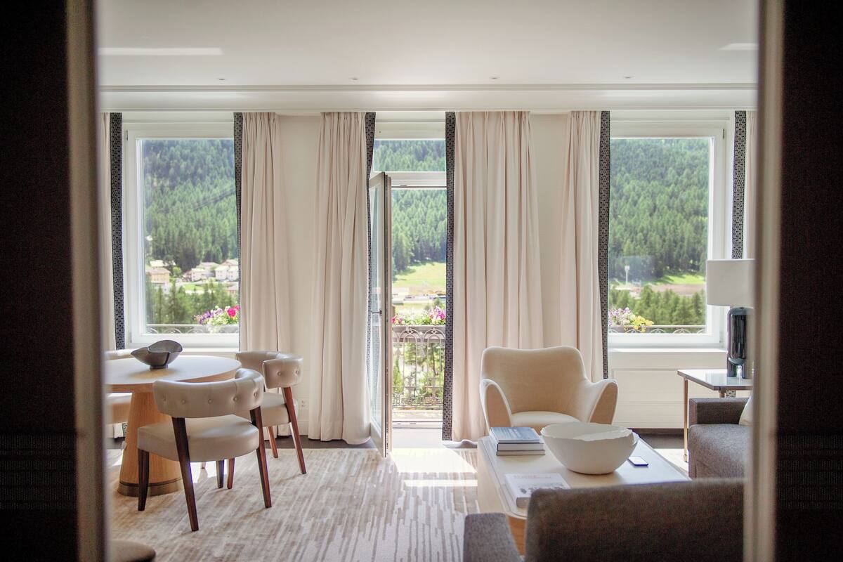 A hotel room with a dining area, a sofa, and a view of a forested area.