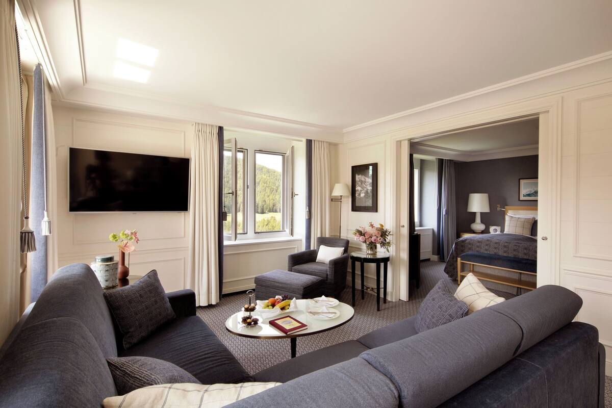 A modern hotel room with a grey sofa set, a round coffee table, and a flat-screen TV mounted on the wall.
