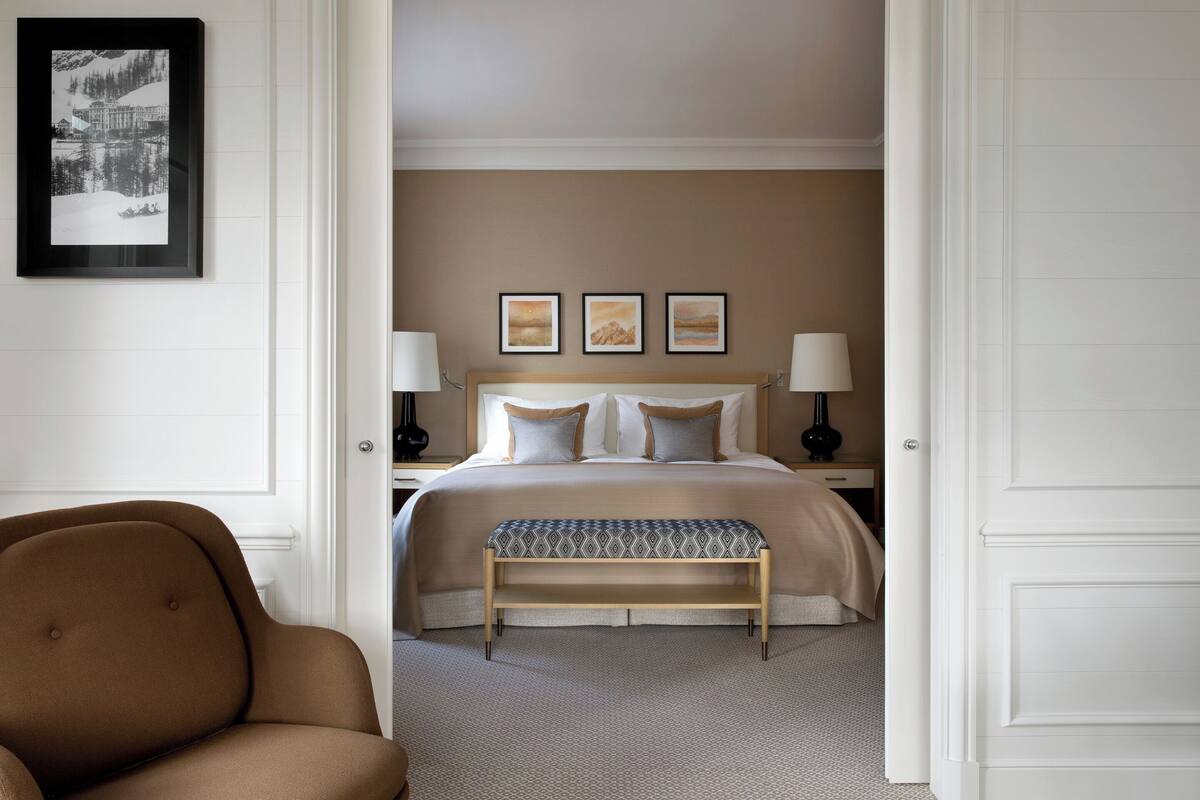 A hotel room with a bed, bedside lamps, a bench, and a framed picture on the wall.