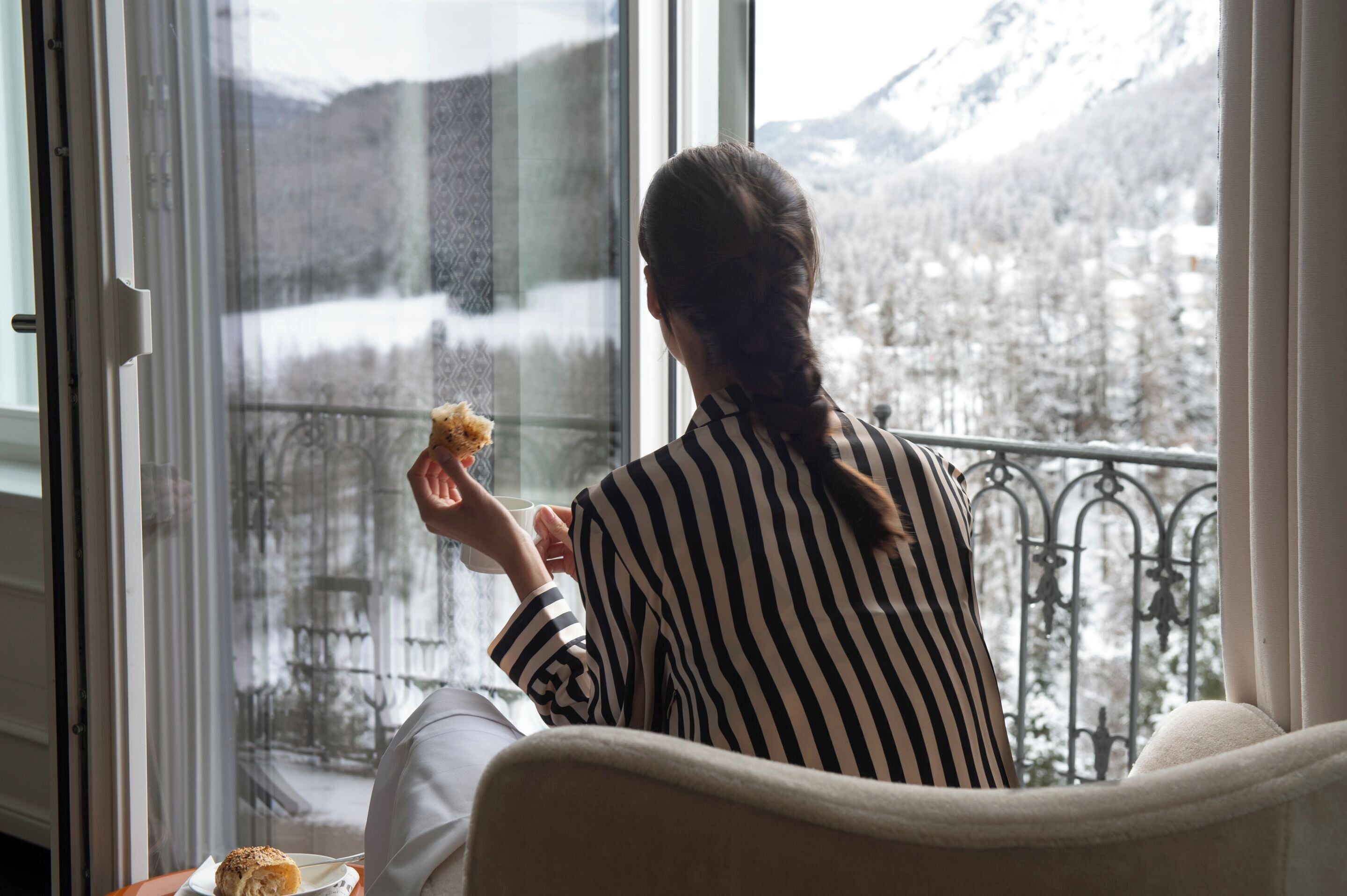 Eine Person sitzt am Fenster mit Blick auf schneebedeckte Berge.