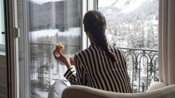 Eine Person sitzt am Fenster mit Blick auf schneebedeckte Berge.