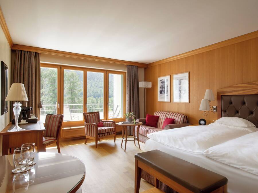 A hotel room with two beds, a dining table, a small round table, and a sofa.