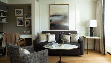 A living room with a sofa, armchair, and coffee table. There is a desk with a computer and a lamp.