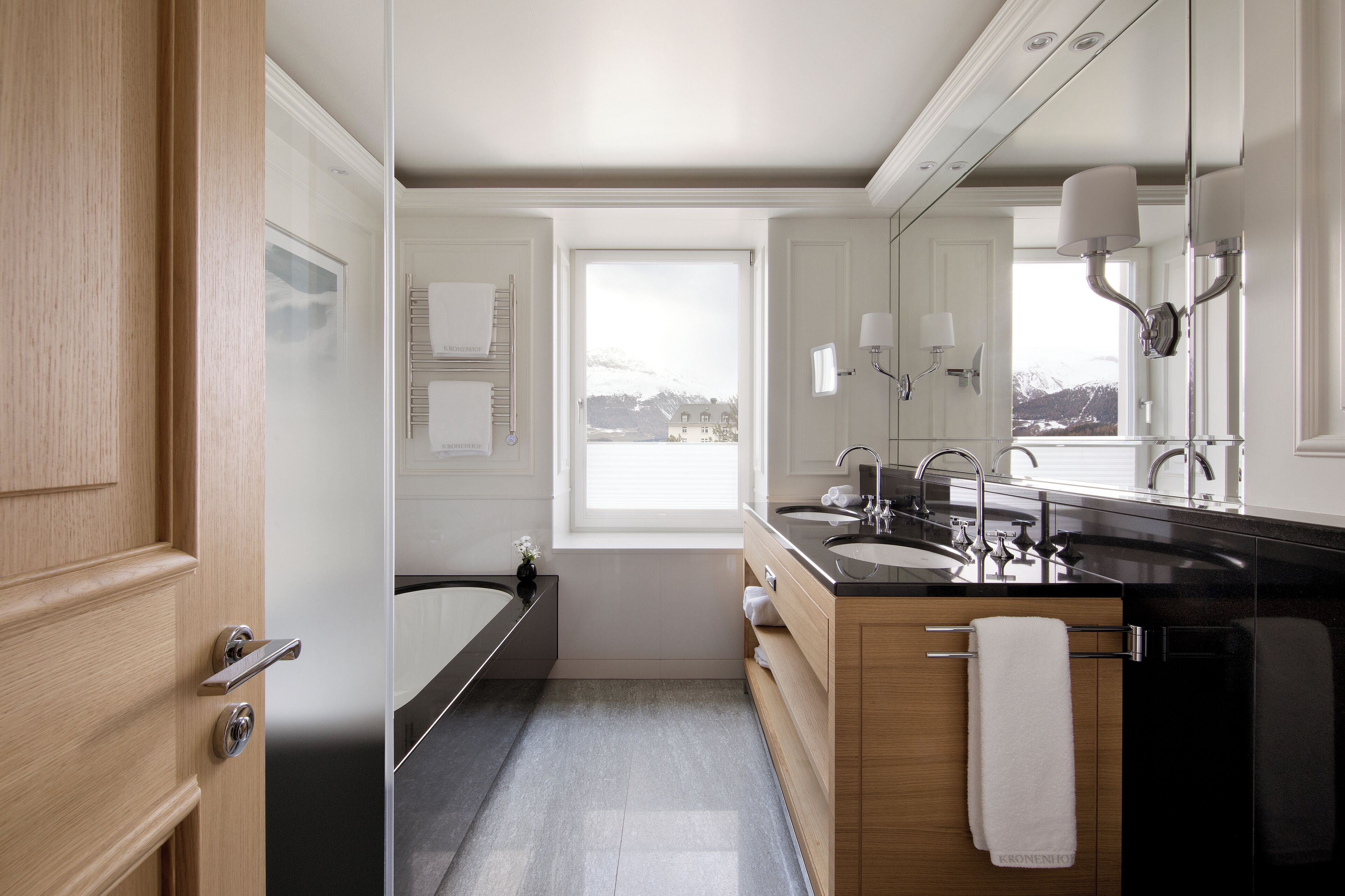 Een moderne badkamer met een badkuip, twee wastafels en een grote spiegel.