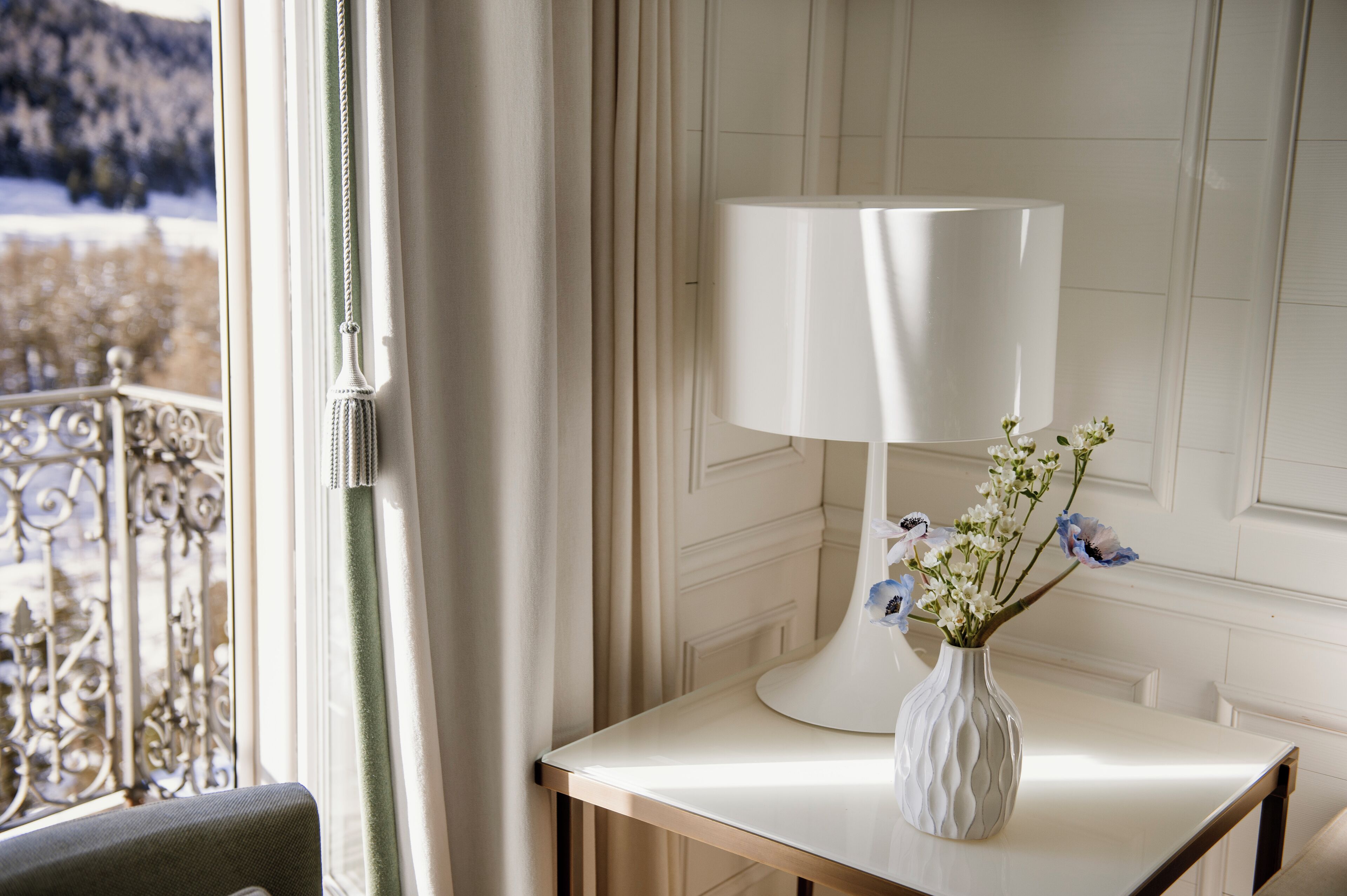 Una habitación con una mesa blanca, una lámpara blanca y un florero con flores.