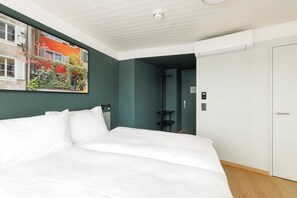 Habitación de hotel con una cama grande, una puerta, un estante en la pared y un cuadro de un edificio con flores.