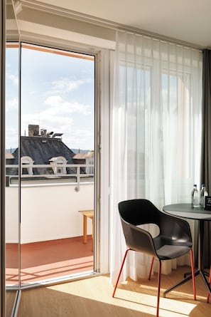 A room with a sliding glass door leading to a balcony, a round table with two chairs, and a small stool.