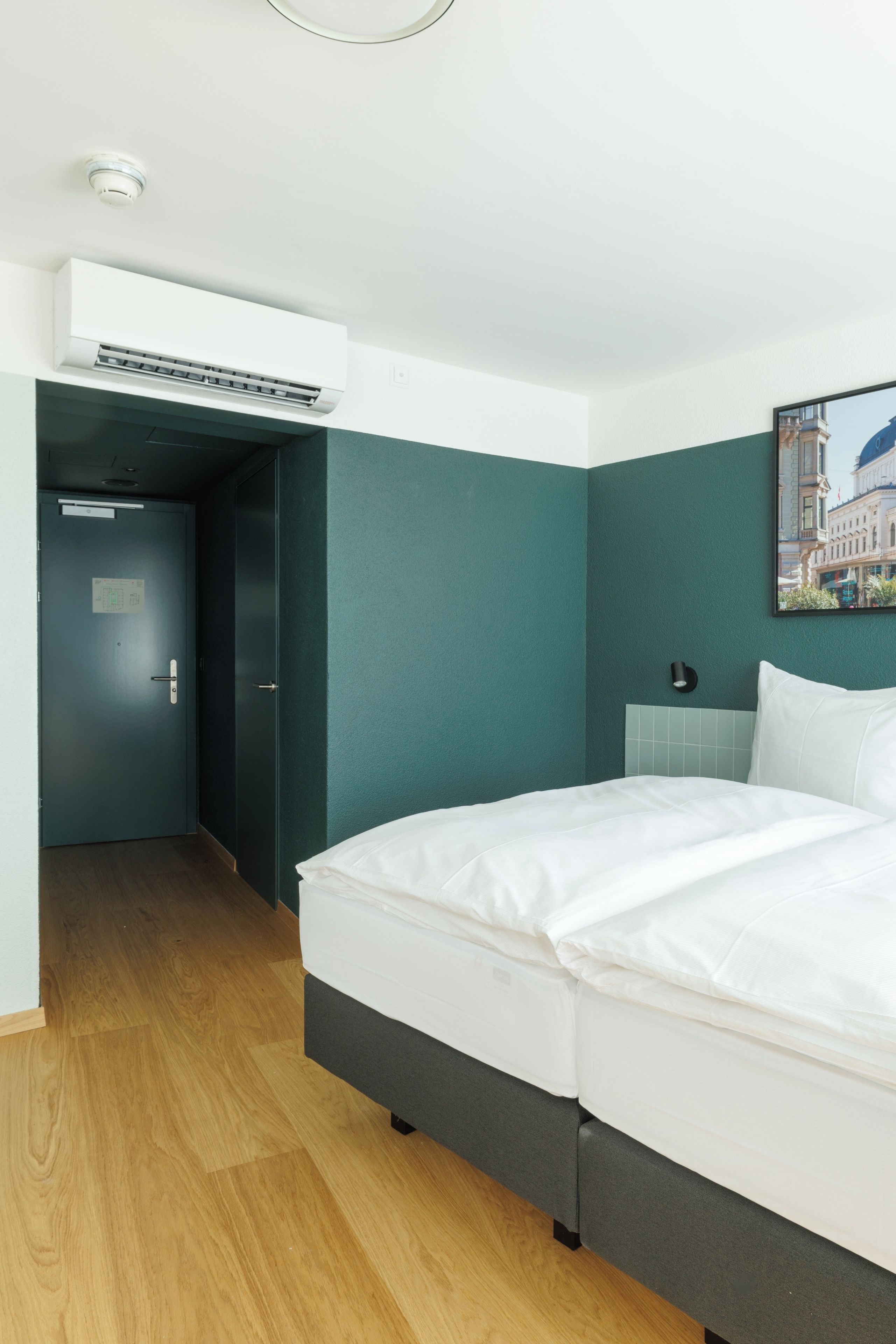 A hotel room with a bed, a door, and an air conditioning unit.