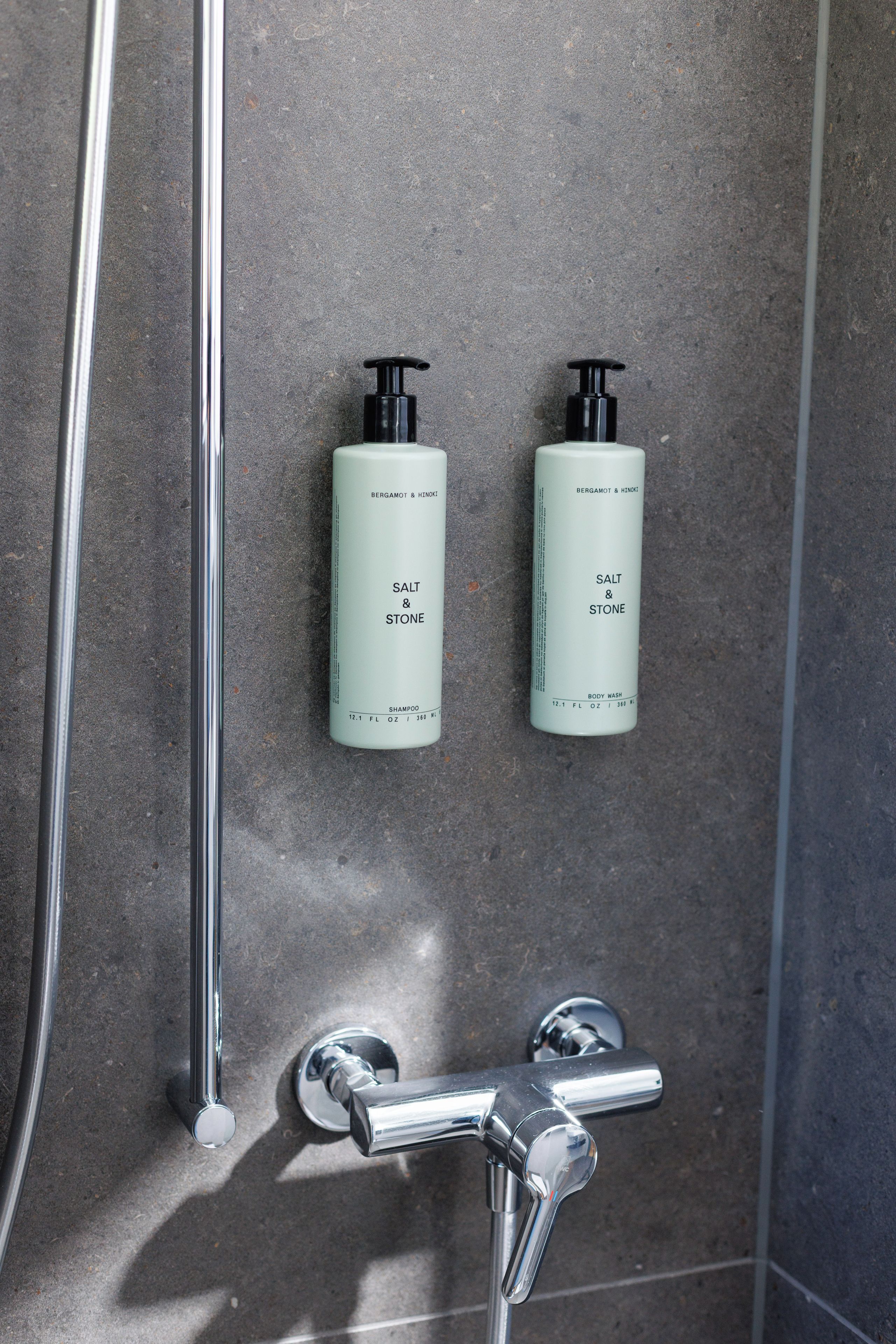 A bathroom with two bottles of shampoo and a showerhead.