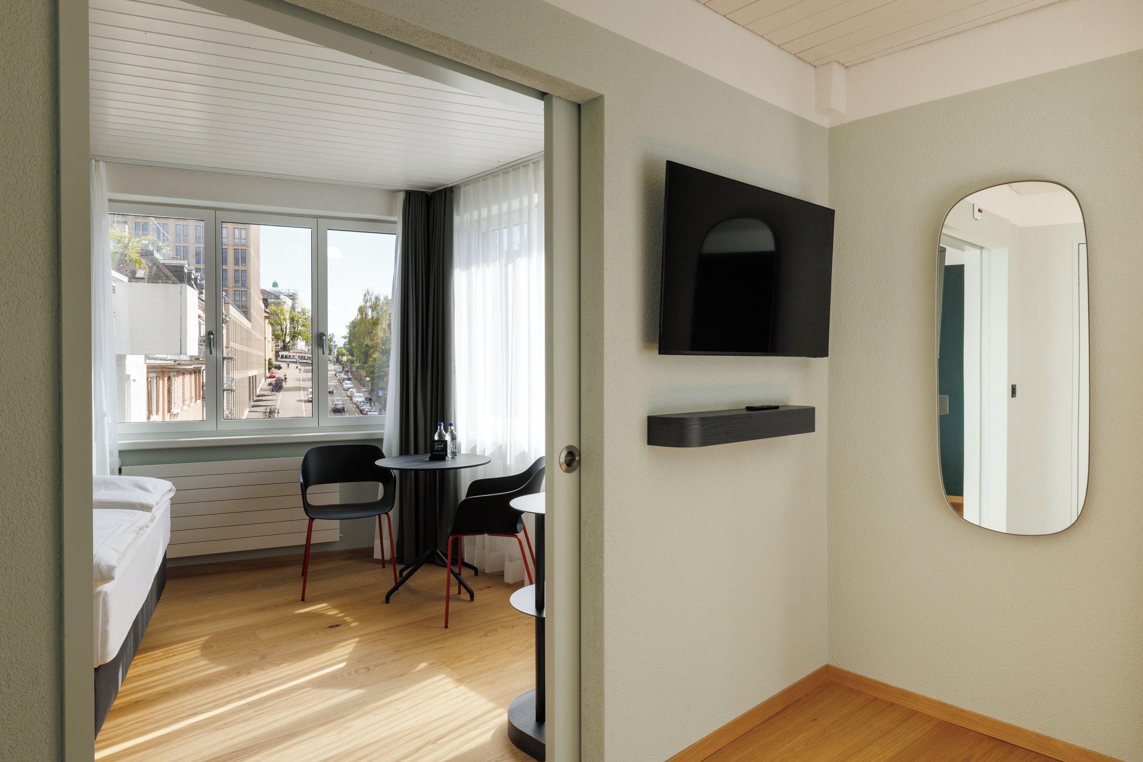 Une chambre d’hôtel avec un lit, une petite table avec des chaises, une télévision et un miroir.