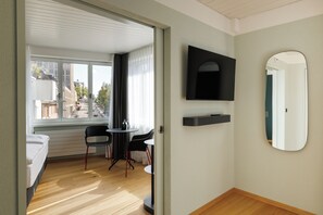 A hotel room with a bed, a small table with chairs, a TV, and a mirror.