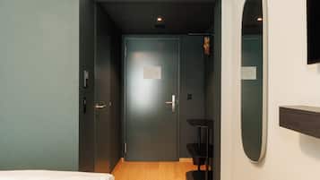 Ein Hotelzimmer mit Bett, Schreibtisch, Stuhl, Klimaanlage und Spiegel an der Wand.