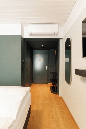 A hotel room with a bed, a desk, a chair, an air conditioning unit, and a mirror on the wall.