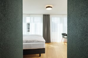 A modern hotel room with a bed, a chair, and a window with sheer curtains. - Fred Hotel Central (Zürich)